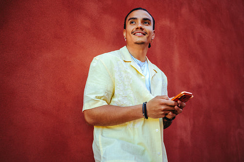 Man holds a smartphone outdoors by a red wall