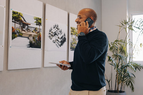 Project manager making a call while reviewing architectural designs in office
