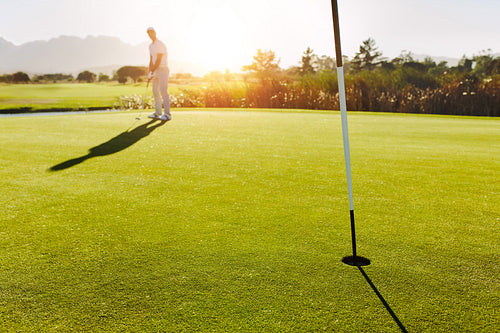 Golf hole and flag in the green field with player in background