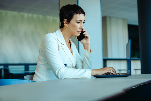 Focused businesswoman working on laptop and phone in modern office