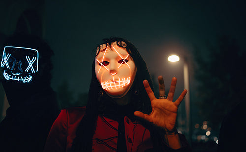 Masked individuals illuminated in neon light during a night city scene