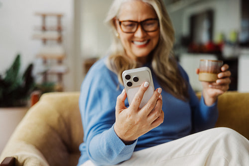 Browsing senior uses a smartphone beside coffee at home