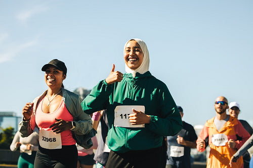Two women running a race with joyful expressions and thumbs up