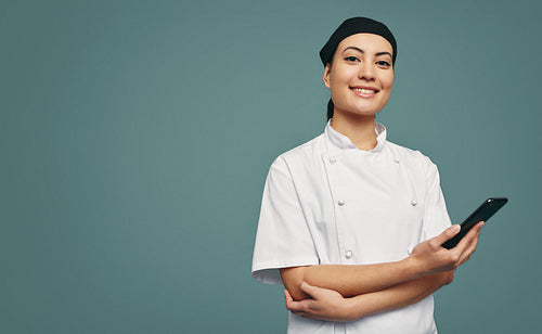 Happy young chef holding a smartphone in a studio
