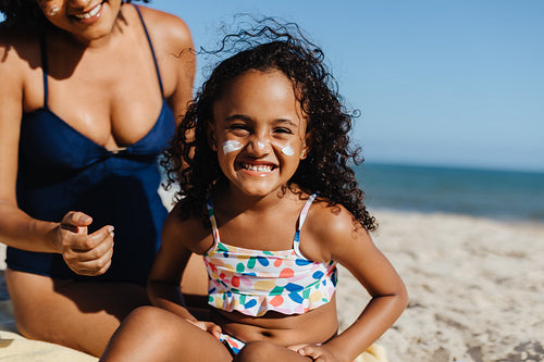 Happy girl applying sunscreen on the beach during a sunny summer day