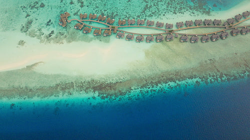 Aerial drone view of luxury overwater bungalows and turquoise ocean waters in a tropical resort