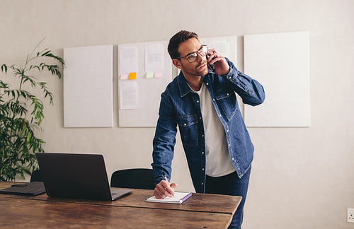 Attentive businessman writing notes during a phone call with his clients