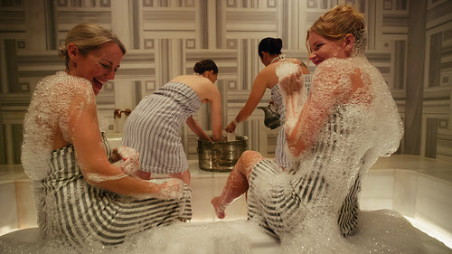 Women enjoying a traditional Hammam spa treatment with luxurious bubbles and laughter for relaxation