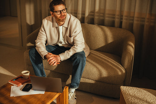 A businessman sits with laptop and papers in a modern business workspace