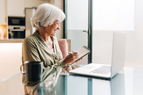 Senior businesswoman making notes during a video conference