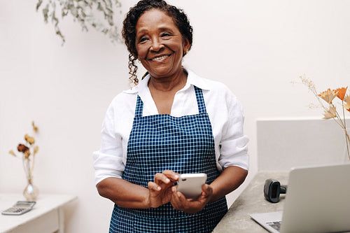 Mature entrepreneur smiling as she uses a smartphone in her flower shop