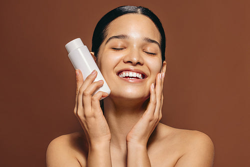 The secret to a youthful glow: Woman holds a bottle of face serum with a big smile