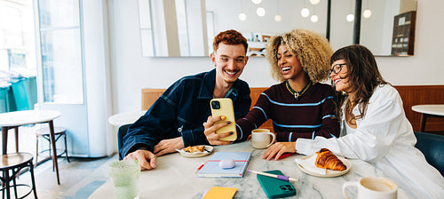 Friends in a cafe looking at phone and laughing