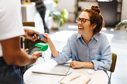 Happy woman using her credit card to make a cashless payment in a coffeehouse