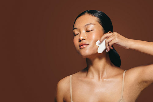 Gua sha for glowing skin: Woman gives herself a facial massage in the midst of her skincare routine