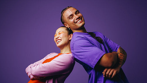 In a smiling studio portrait, friends stand back to back with youthful confidence