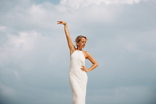 Elegant woman in white dress posing under a vibrant blue cloudy sky