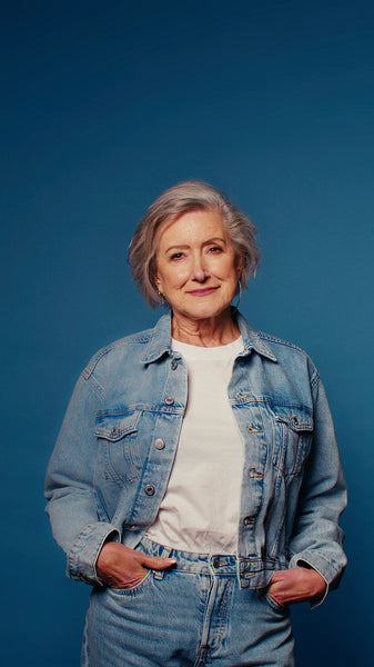 Stylish senior woman in denim jacket and jeans posing confidently on a blue background