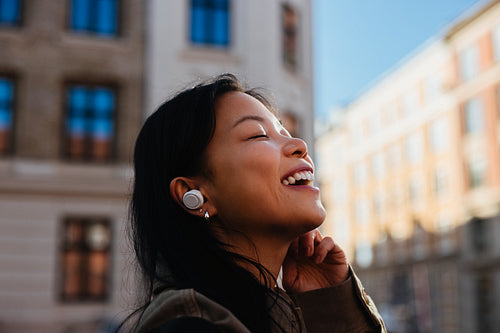 Woman listening with earbuds and smiling in city