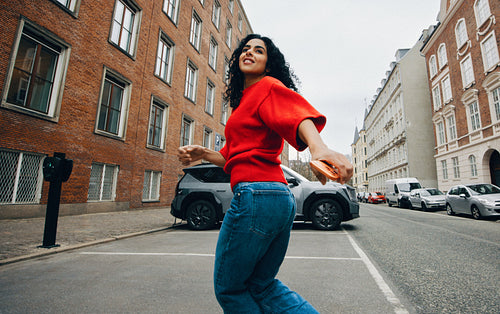 Her woman commuter moment unfolds on a city street as she nears an electric car charger with her phone