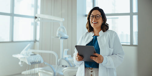 Dentist using tablet and smiling in bright dental clinic