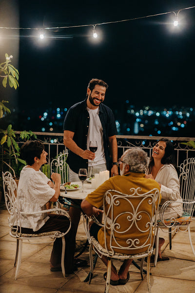 Family enjoying dinner on a balcony under string lights at night