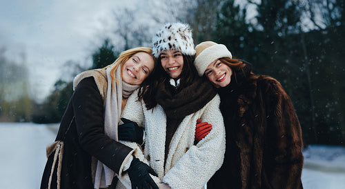 Women friends hug together in snow during winter