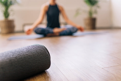 Yoga mat in fitness center with woman meditating at back