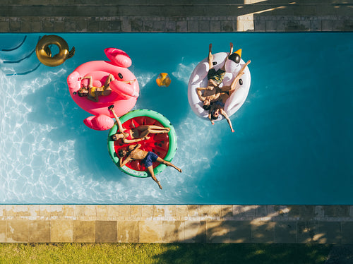 Friends chilling on air mattresses in swimming pool
