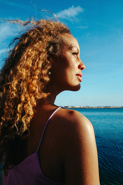 Woman enjoys sunlight on face while gazing over the sea