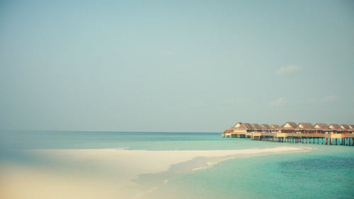 Tropical island resort with overwater bungalows and a white sand beach at sunrise