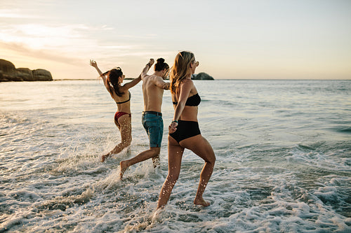 Friends holding hands and running at beach