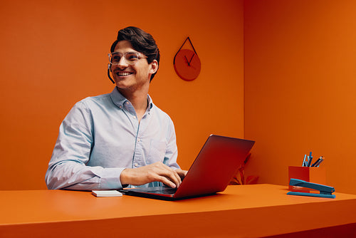 Young male sales representative wearing headset and using laptop in an orange colored office