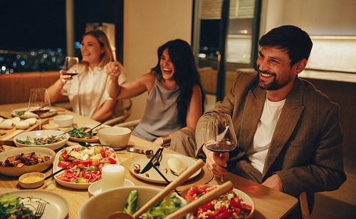 Friends enjoying dinner and wine at a cozy home with warm ambiance