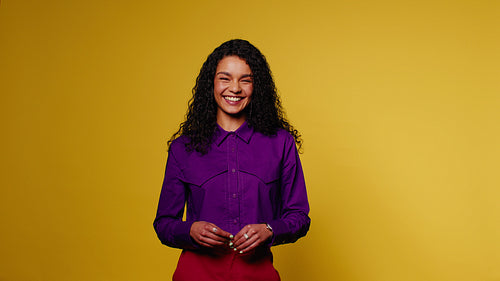 Young woman laughs against a vibrant yellow background in colorful studio portrait