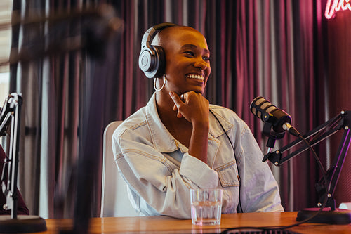 Happy female podcaster recording in studio with professional microphone