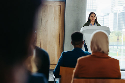 Young businesswoman speaking at a conference, giving a presentation to a diverse audience in a modern workshop setting
