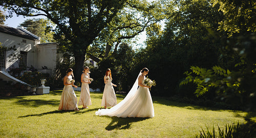 Bride and bridesmaids walking in sunlight at a garden wedding ceremony