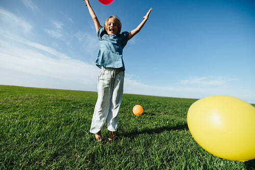Child jumping with balloons in open park
