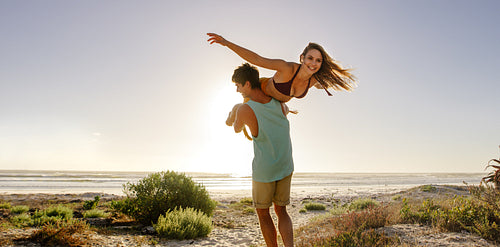 Man carrying his girlfriend on his back walking on the beach