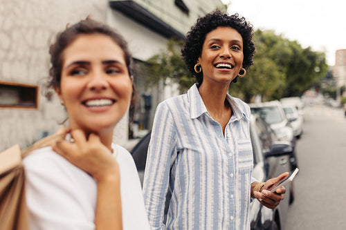 Two cheerful young women waiting for a taxi in the city