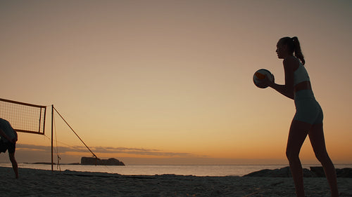 Female beach volleyball player in silhouette serves for victory