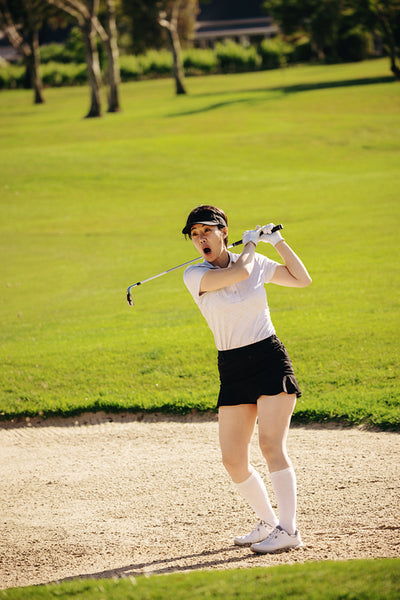 Surprised woman golfer reacting to her swing on the golf course during her shot from sand bunker.