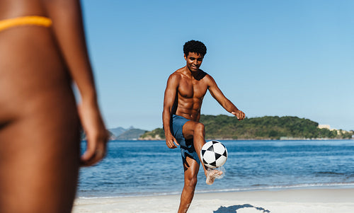 Young male playing soccer on a beach with blue sky and ocean in the background