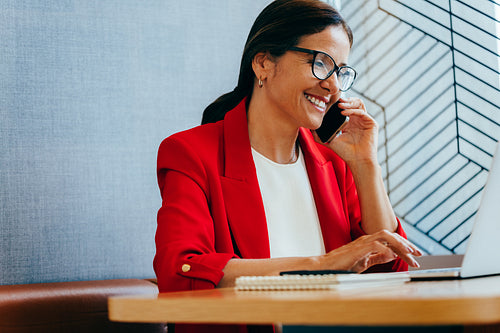 Businesswoman in a red jacket working while on a smartphone call
