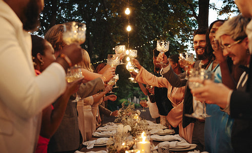 Group of friends making a toast at outdoor dinner party under string lights