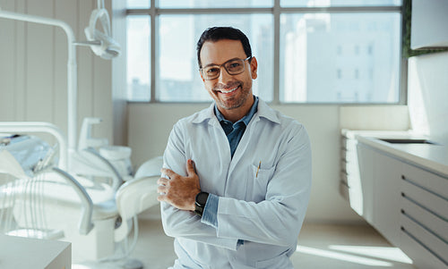 Confident dentist stands with crossed arms in a bright dental clinic