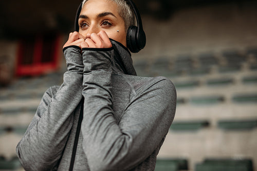 Woman in sweatshirt standing in a stadium listening to music