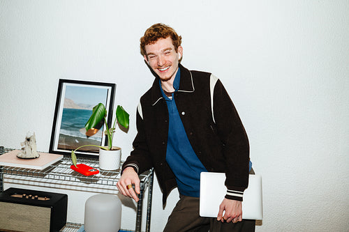 A smiling man stands at home with a laptop for remote work.