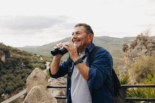 Adventurous senior man using binoculars while hiking